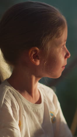 kid looks out of transparent wall of tent. calm child looks into distance dreamily resting in glamping at dawn. happy kid sits in comfortable chair