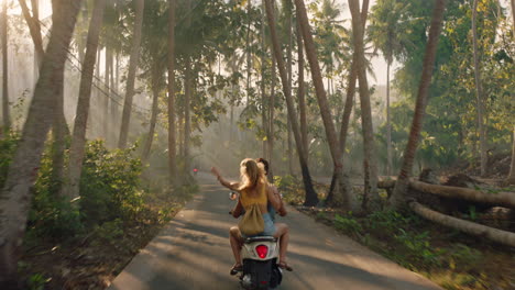 happy couple riding scooter on tropical island girlfriend having fun with arms raised exploring beautiful travel destination on motorcycle with boyfriend