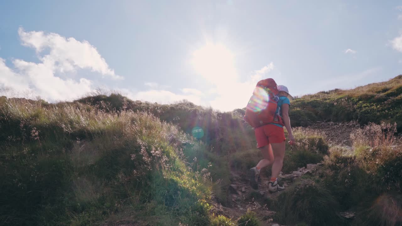 mujer mochilera turística ascendiendo la montaña en un día soleado