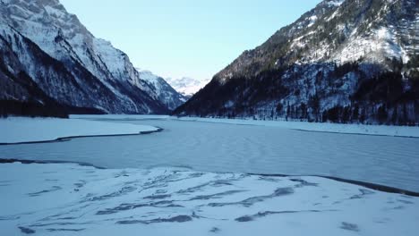 frozen, ice-covered lake during wintertime in switzerland mountains, aerial