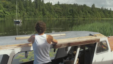 wide shot young man removing masking tape from cabin roof of wooden boat