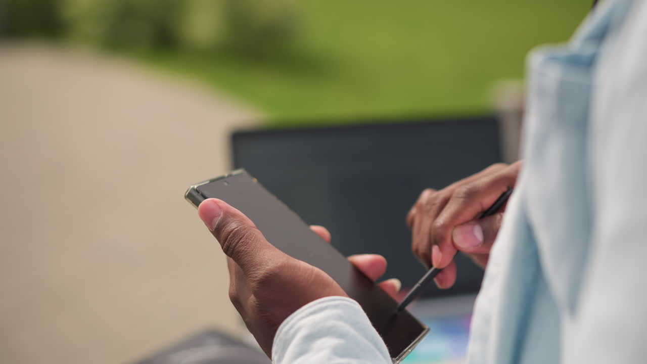 black DJ adjusting mix with stylus near laptop, openair park booth, hands scrolling playlist, checking levels on controller, sunlit green background, chill ambient vibe, focused creative session