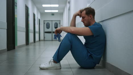 stressed surgeon staying clinic hallway after operation. doctor sitting alone.