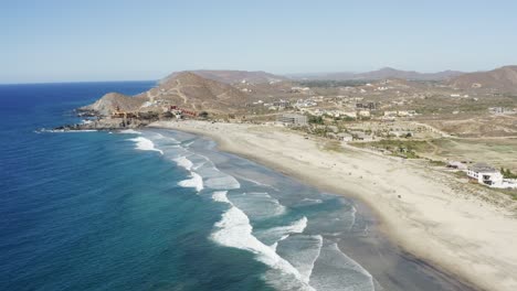 Weitwinkel-Zeitlupenaufnahme-Der-Strandwasserwellen-Von-Los-Cerritos,-Die-An-Einem-Sonnigen-Tag-In-Mexiko-In-Einer-Bergkette-In-Der-Nähe-Einer-Küste-Oder-Einer-Stadt-In-Den-Sand-Stürzen