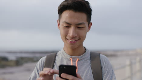 charming young asian man using phone standing on beach texting