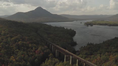 Old-trestle-close-up,-leading-to-a-distant-mountain-with-autumn-foliage-AERIAL-PUSH-IN