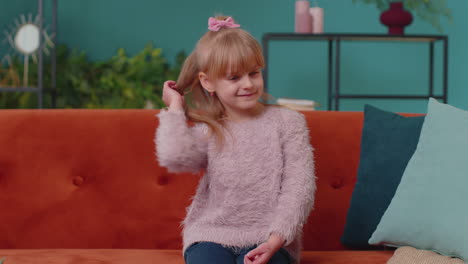 Portrait-of-little-adorable-child-girl-sitting-alone-on-sofa-at-home-looking-at-camera-and-smiling