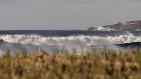 Waves-crash-against-the-shore-in-extreme-slow-motion-with-grass-and-vegetation-foreground