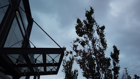 Low-angle-time-lapse-of-an-empty-office-building-entrance,-lights-coming-on-and-off,-set-against-a-stormy-sky