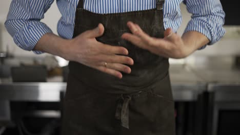 el panadero masculino se limpia las manos y el delantal de la harina y pone las manos en las caderas