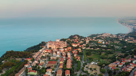 flying over small historical town in marche, italy on top the cliff over the adriatic sea at dusk