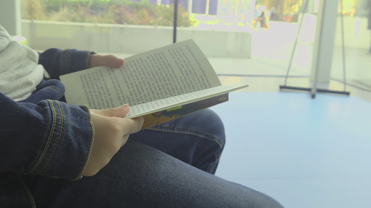 Close-up view of a child's hands holding an open book indoors. Natural color grade and sharp lifestyle textures in a 2026 style