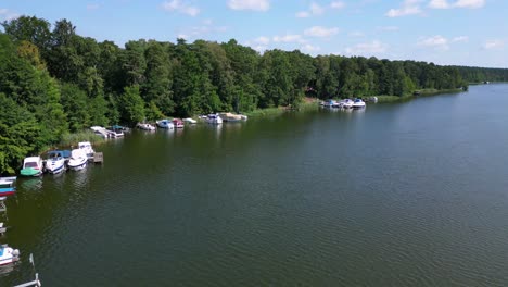 motorboats at the jetty on a calm lake surrounded by green forest on a sunny summer day in germany. beautiful aerial view flight descending drone