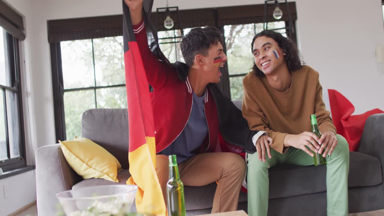 feliz pareja masculina diversa viendo televisión con banderas nacionales y apoyando