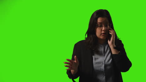 Frustrated-Young-Businesswoman-Wearing-Glasses-Talking-On-Mobile-Phone-Against-Green-Screen-Studio-Background-2