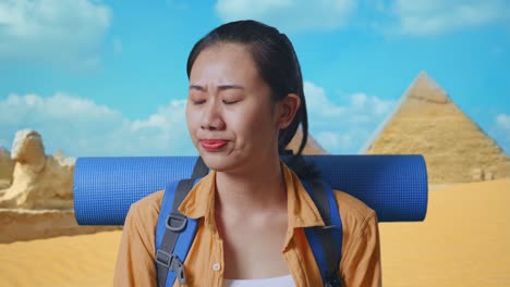 close up of asian female hiker with mountaineering backpack shaking her head and making unsatisfied face while traveling in pyramid of giza