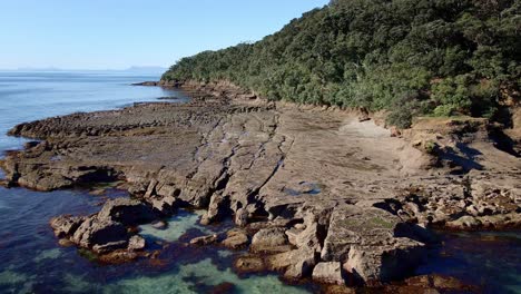 aproximación aérea hacia formaciones rocosas cinceladas y erosionadas de la costa de la isla de cabra en un día soleado, nueva zelanda