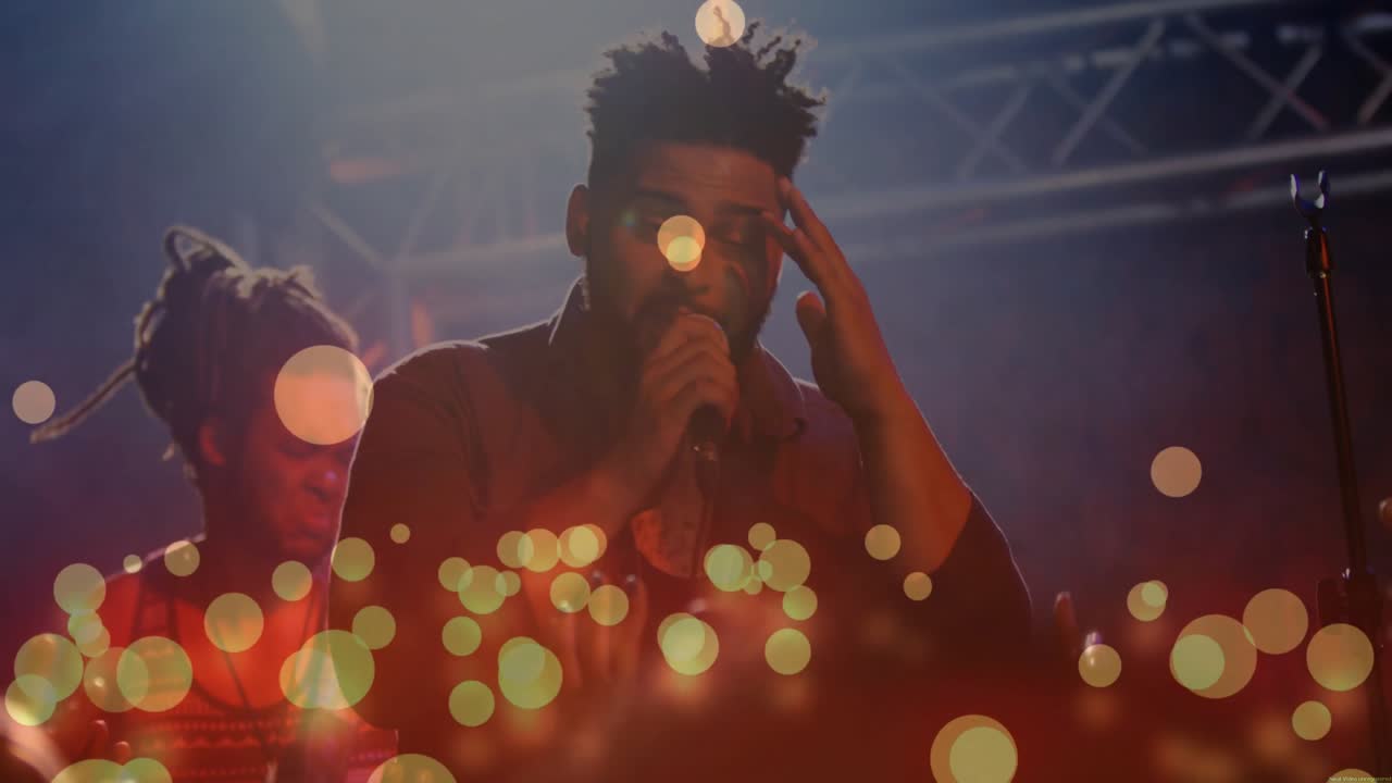 Cantante uomo che sale sotto i riflettori cantando musica dal vivo mentre il chitarrista annuisce, con sovrapposizione bokeh.