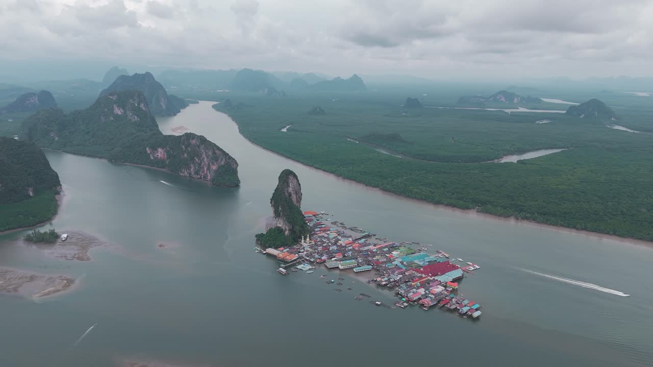 la toma de un dron captura el pequeño pueblo flotante de kon panyi enclavado en medio de una exuberante vegetación, rodeado de altas montañas y un mar azul brillante