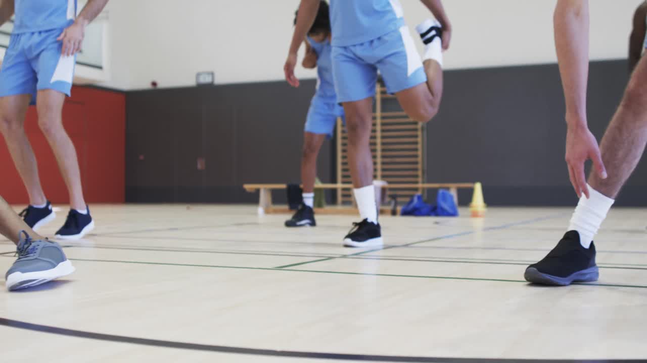 Pernas de jogadores de basquete masculinos diversos alongando-se em sessão de treino, em câmera lenta.