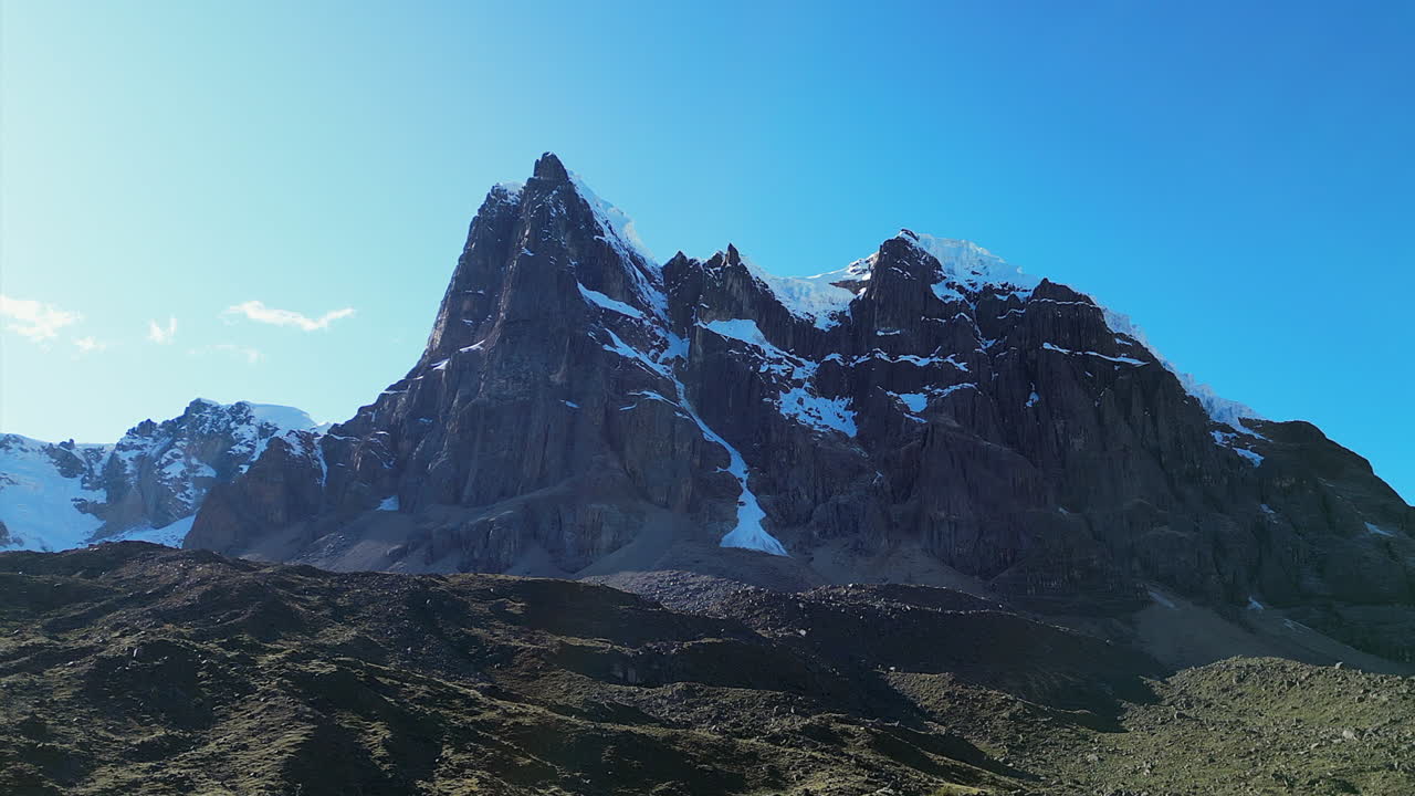 Flyover rough glacial terrain below rocky Cuyoc Mountain peak in Peru