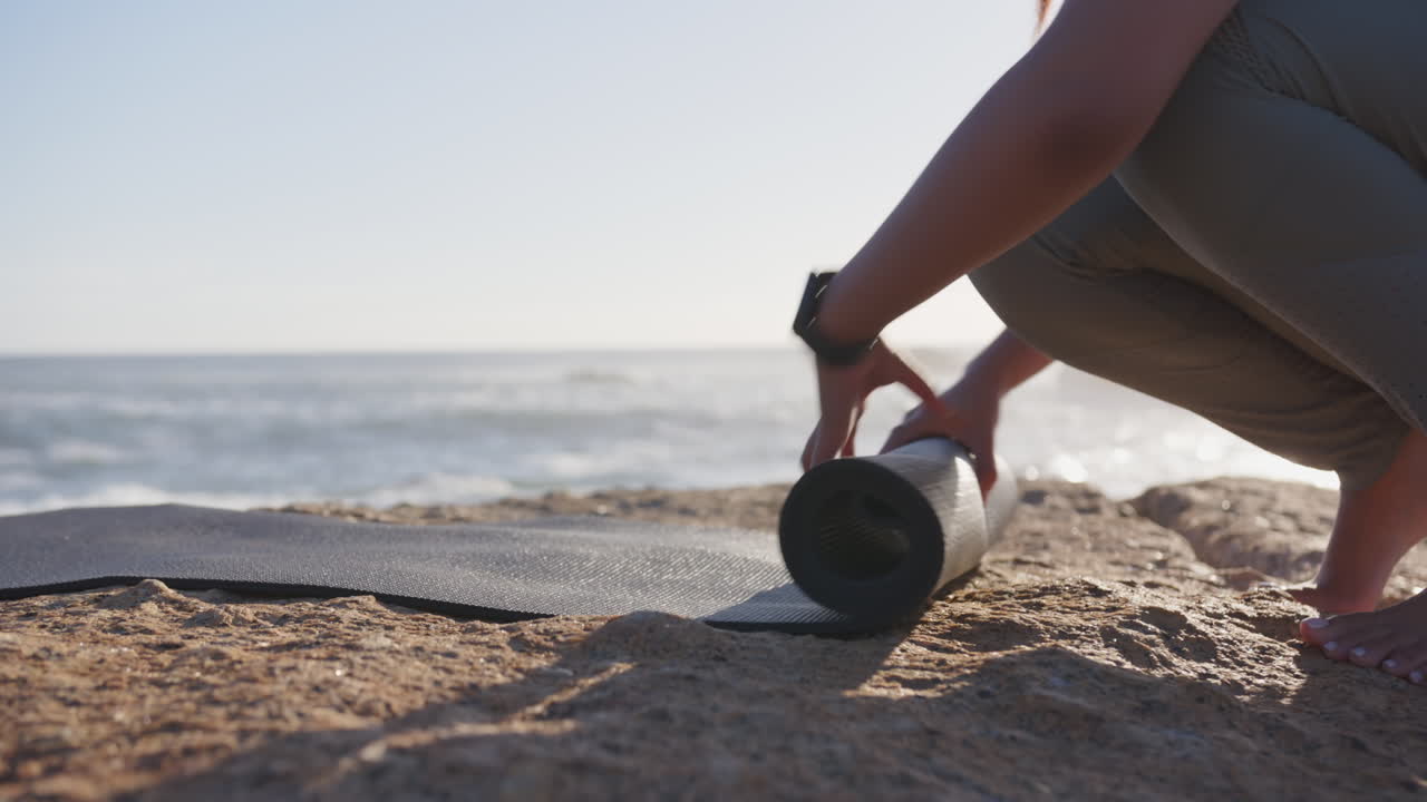 Rolling up yoga mat on beach, asian woman preparing for outdoor exercise session