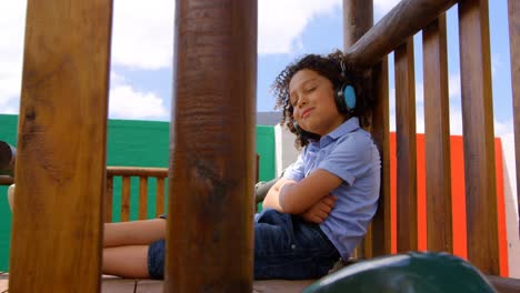 vista lateral de una colegiala de raza mixta escuchando música con auriculares en el patio de recreo de la escuela 4k