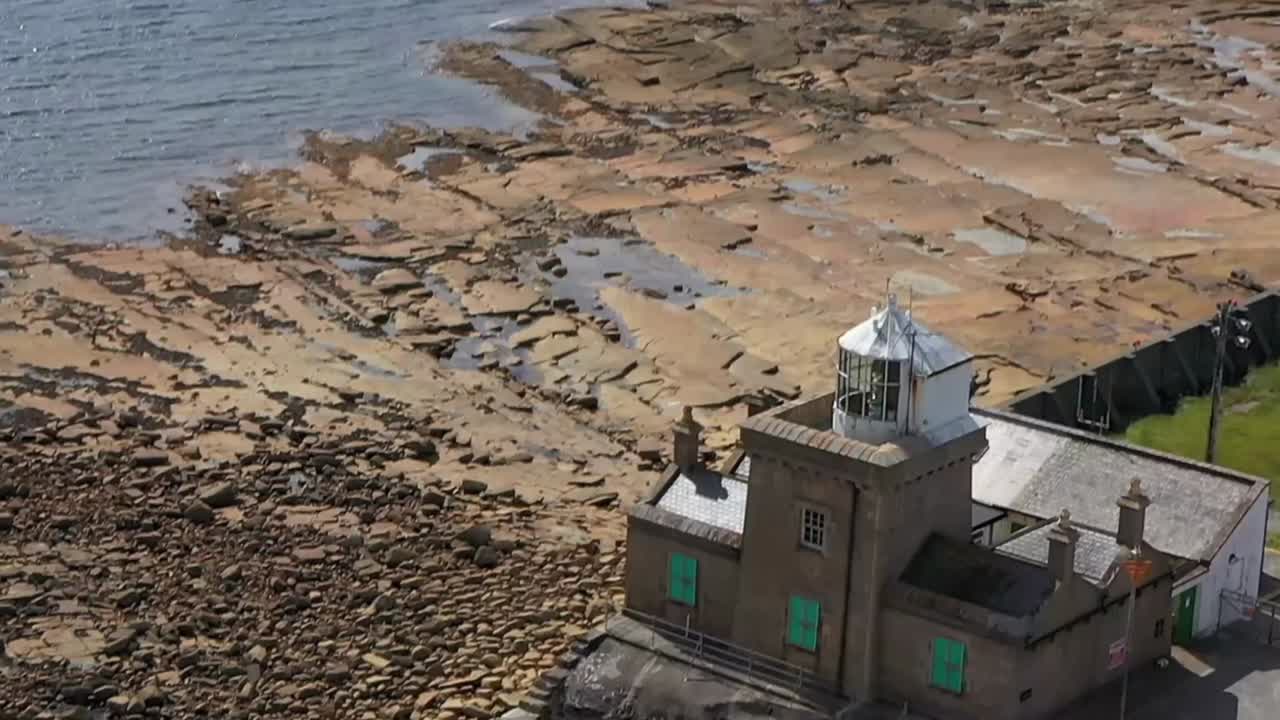 Ripresa aerea discendente in cui il faro di Blacksod emerge sullo sfondo della costa rocciosa e delle acque dell'Atlantico
