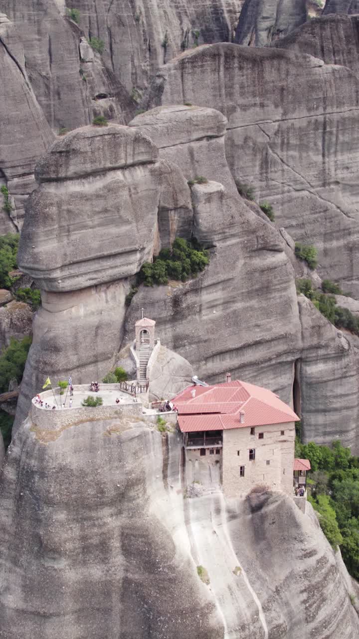 Vertical aerial revealing Saint Nicholas Anapafsas Monastery perched atop a cliff in Meteora, Greece