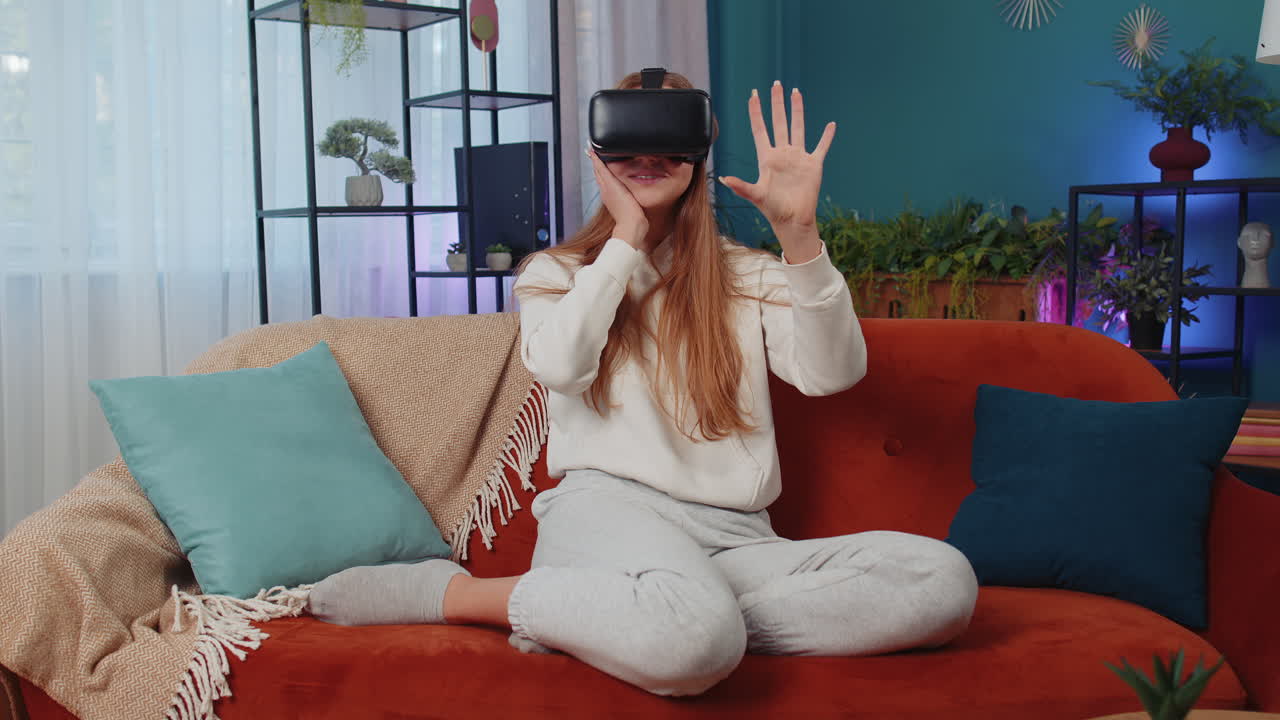 una mujer joven usa gafas de realidad virtual en casa, disfrutando del concepto de video moviendo las manos en el aire