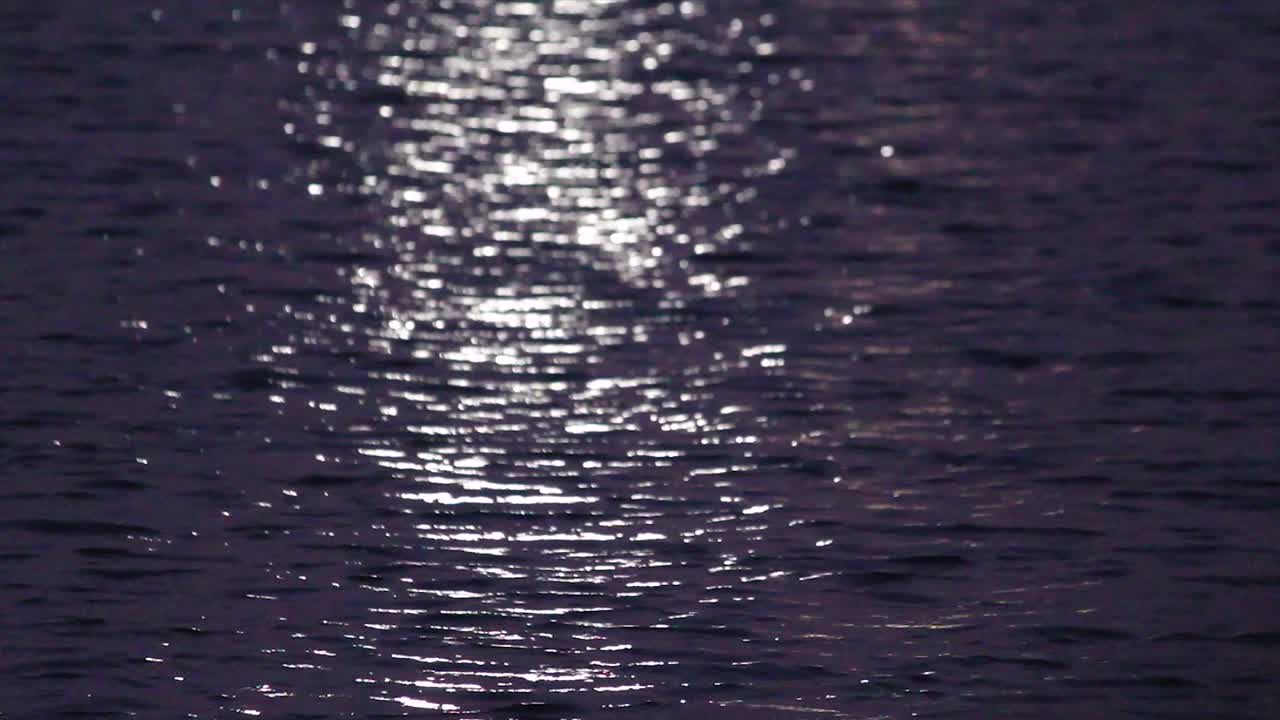Captivating close-up of water surface at night with shimmering moon or city light reflections. Ideal for calming, mysterious, peaceful and abstract water themes.
