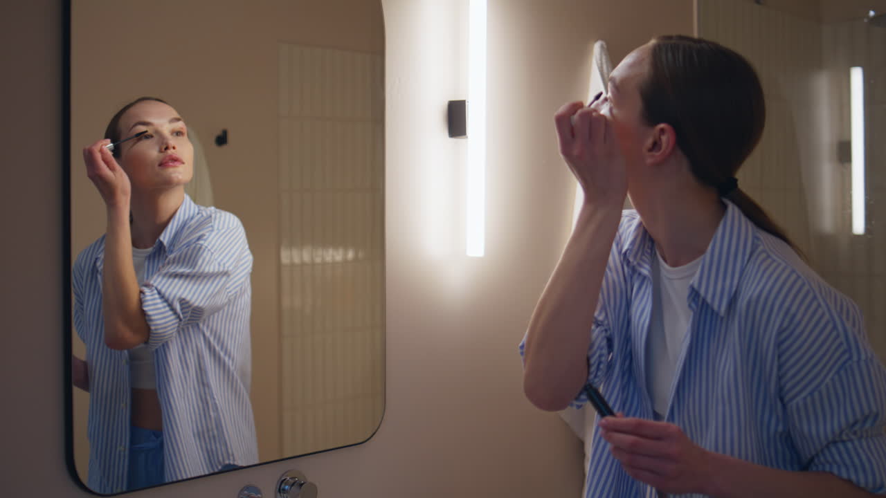 Riflesso di una donna che si spazzola le ciglia nel bagno di casa. Ragazza alla moda che si trucca.