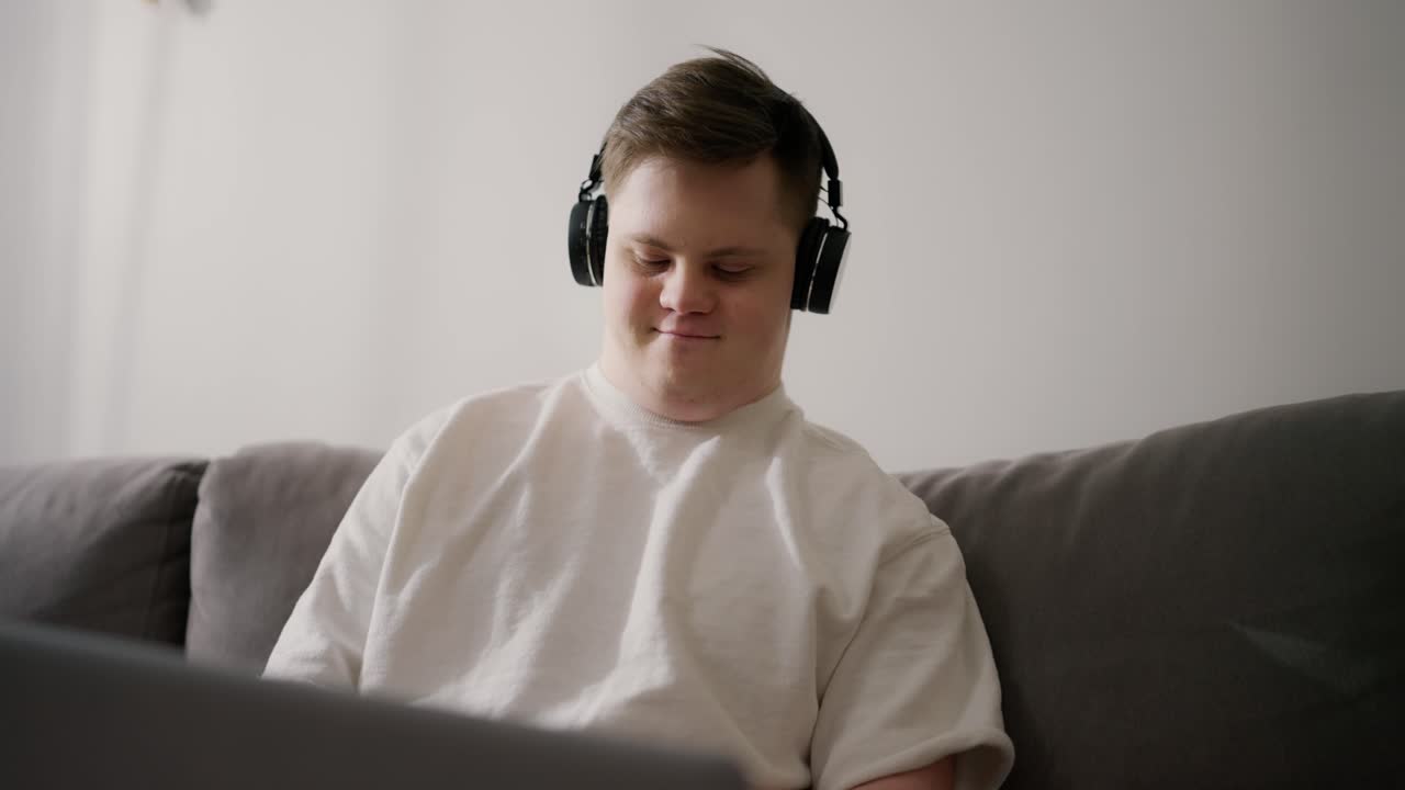 Man with down syndrome at home in headphones using laptop