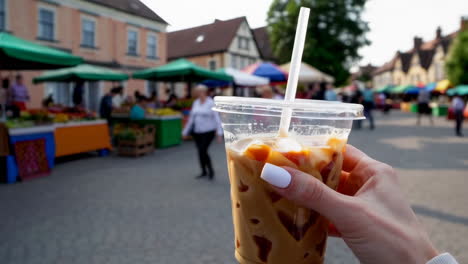hand holding iced coffee at a bustling outdoor market