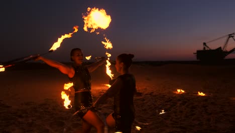 a group of men and woman fire show at night on the sand against the background of fire and tower cranes