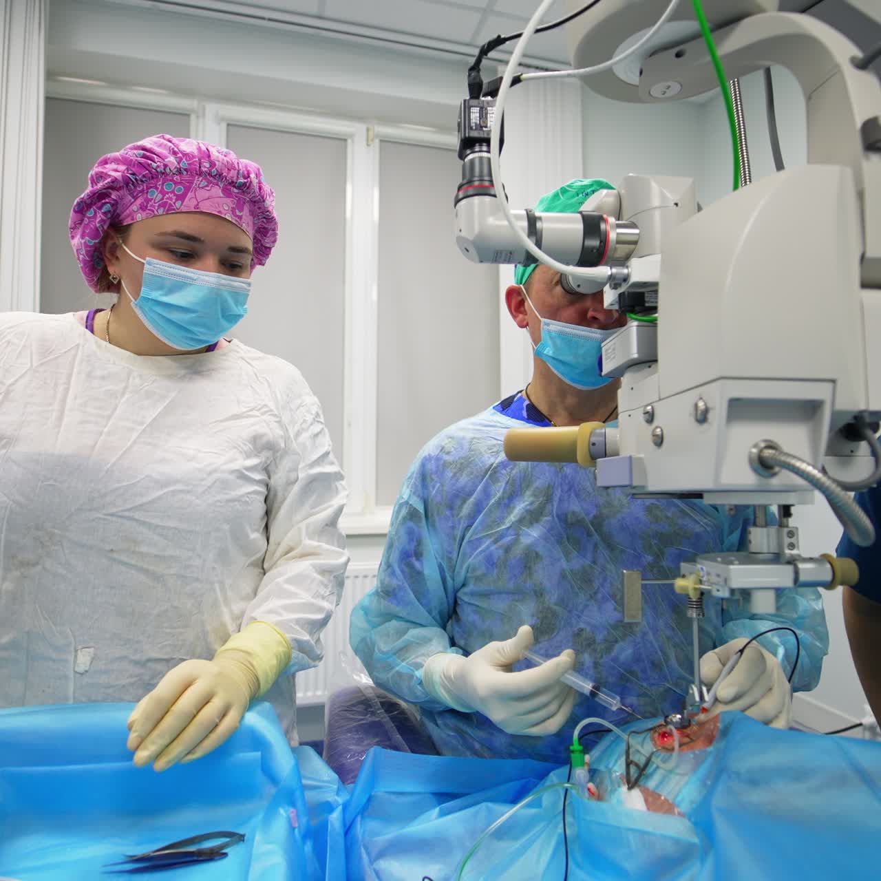 Approaching the team of medics performing the eye operation. Chief surgeon conducts surgery looking in microscope assisted by two medics