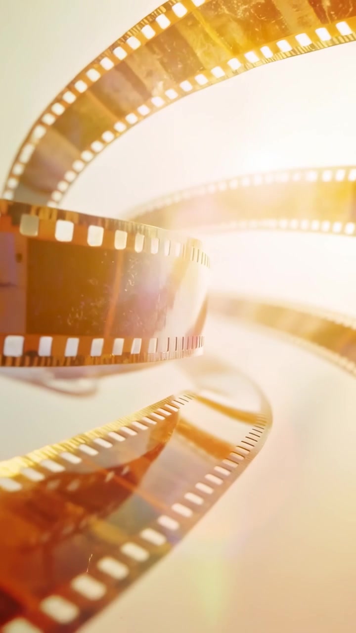 Video verticale: Un bagliore che sale, un nastro di pellicola ambrato che si avvolge a spirale su uno sfondo, mostrando fotogrammi e perforazioni.