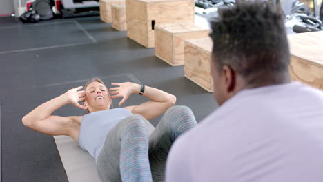 una joven blanca en forma hace ejercicios en el gimnasio, guiada por un hombre afroamericano.