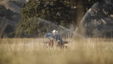farmer reaches down from his atv to fix his water sprinkler