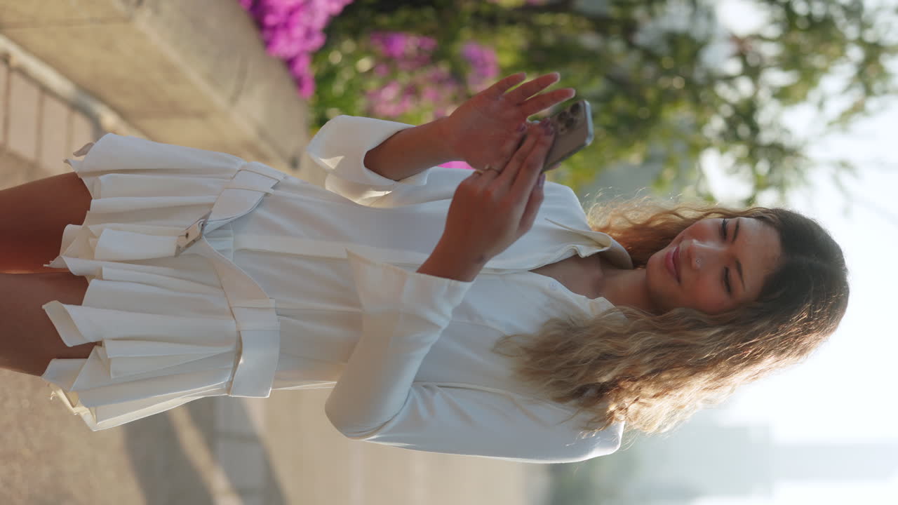 Young woman using smartphone outdoors in a white dress