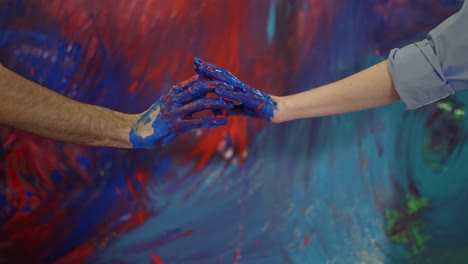 Couple-hands-in-paints-in-front-colorful-canvas,-touching-motion