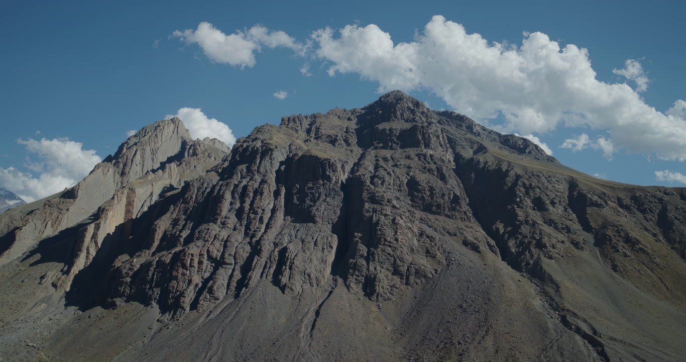 Cinematic drone aerial of a rugged mountain slopes and rocky ridges under clear blue sky, revealing vast natural terrain and dramatic textures, perfect for adventure and immersive visual storytelling.
