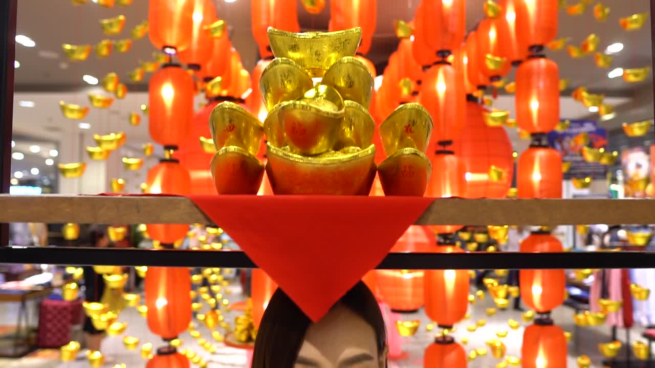 linternas chinas de color naranja brillante y decoración dorada en una tienda departamental, luego descienden en un pedestal para revelar a una mujer asiática debajo