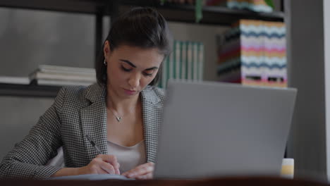 mujer de negocios analizando el gráfico y escribiendo en el portátil. trabajo remoto mujer joven con gafas escribe notas en el portapapeles y escribiendo en el teclado del portátil