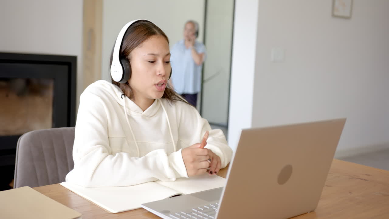 Using laptop and wearing headphones, girl studying at home with notebook nearby, copy space
