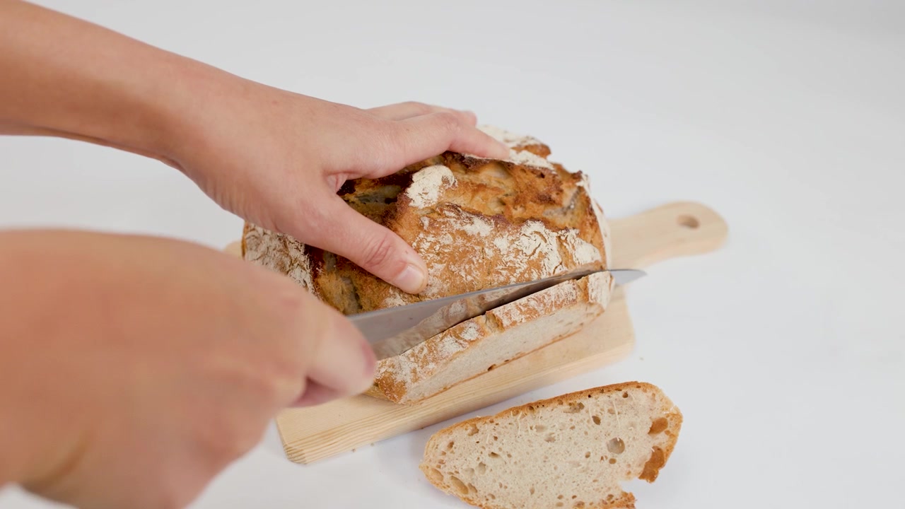 Person Slicing Fresh Crusty Sourdough Bread on Wooden Board