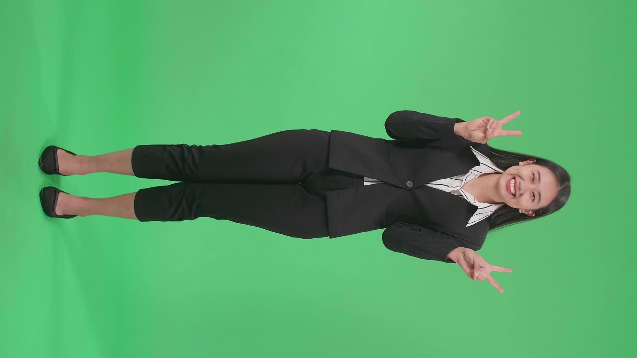 Full Body Of An Asian Business Woman Showing Gesture Peace And Smiling While Standing On Green Screen In The Studio