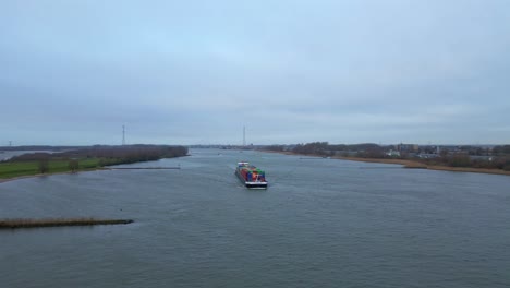 Aerial-View-Of-Cargo-Container-Ship-Approaching-Along-Beneden-Merwede-On-Overcast-Day