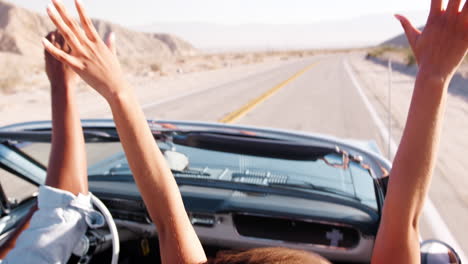 Couple-driving-open-top-car-raising-their-hands-in-the-air