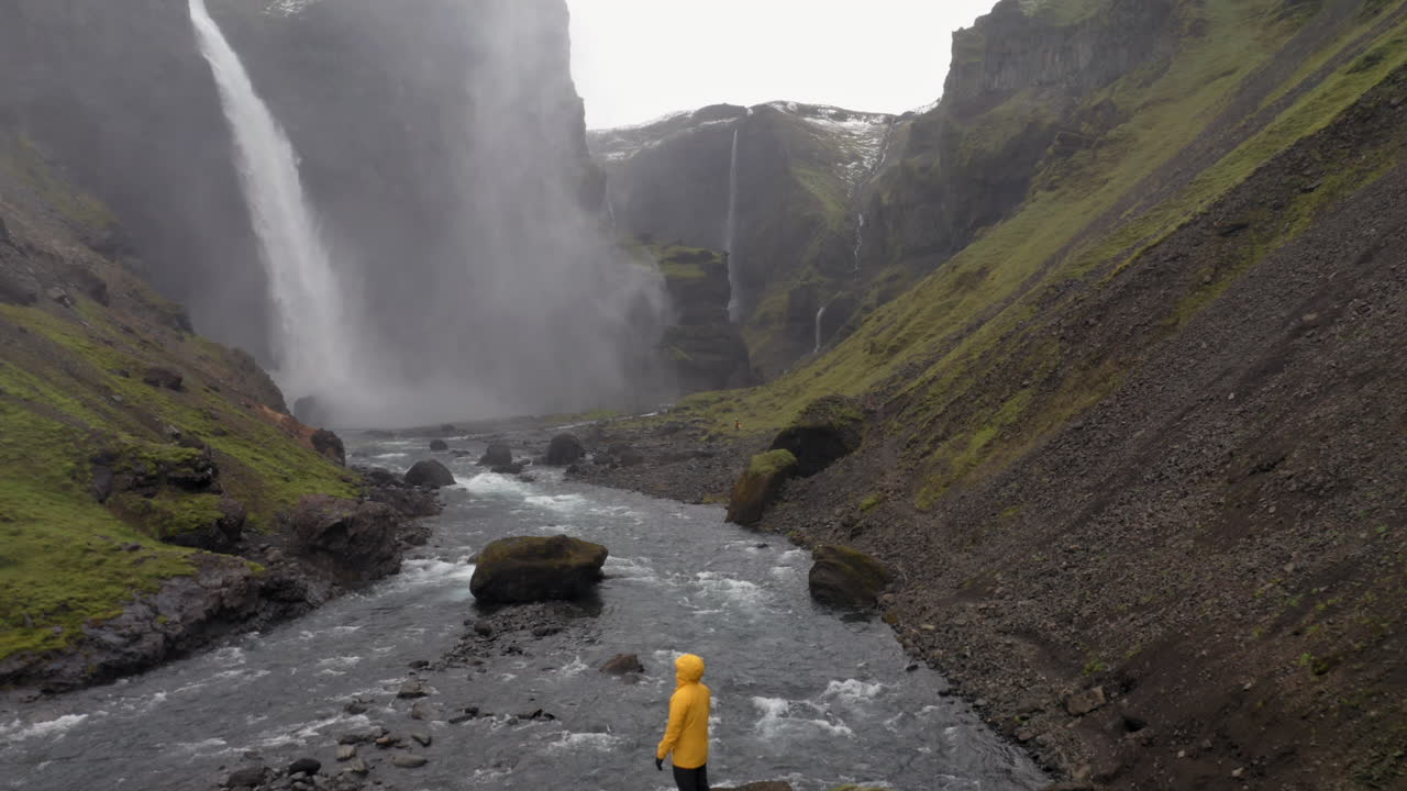 retroceso de drones para revelar a una persona de pie sobre una roca, cerca de la cascada de haifoss en islandia